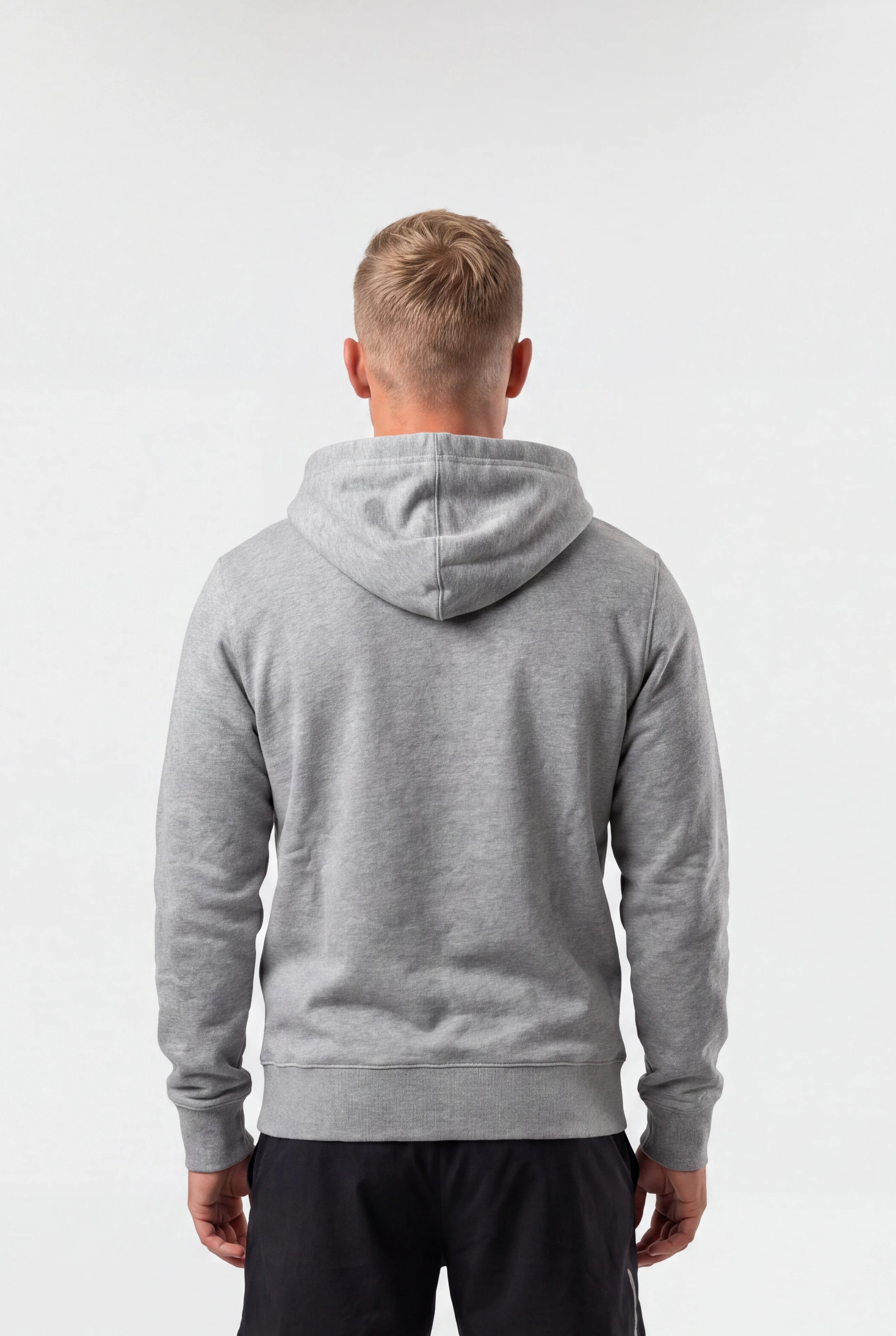 A man viewed from behind wearing a heather gray pullover hoodie and black athletic shorts, standing against a plain white studio background.
