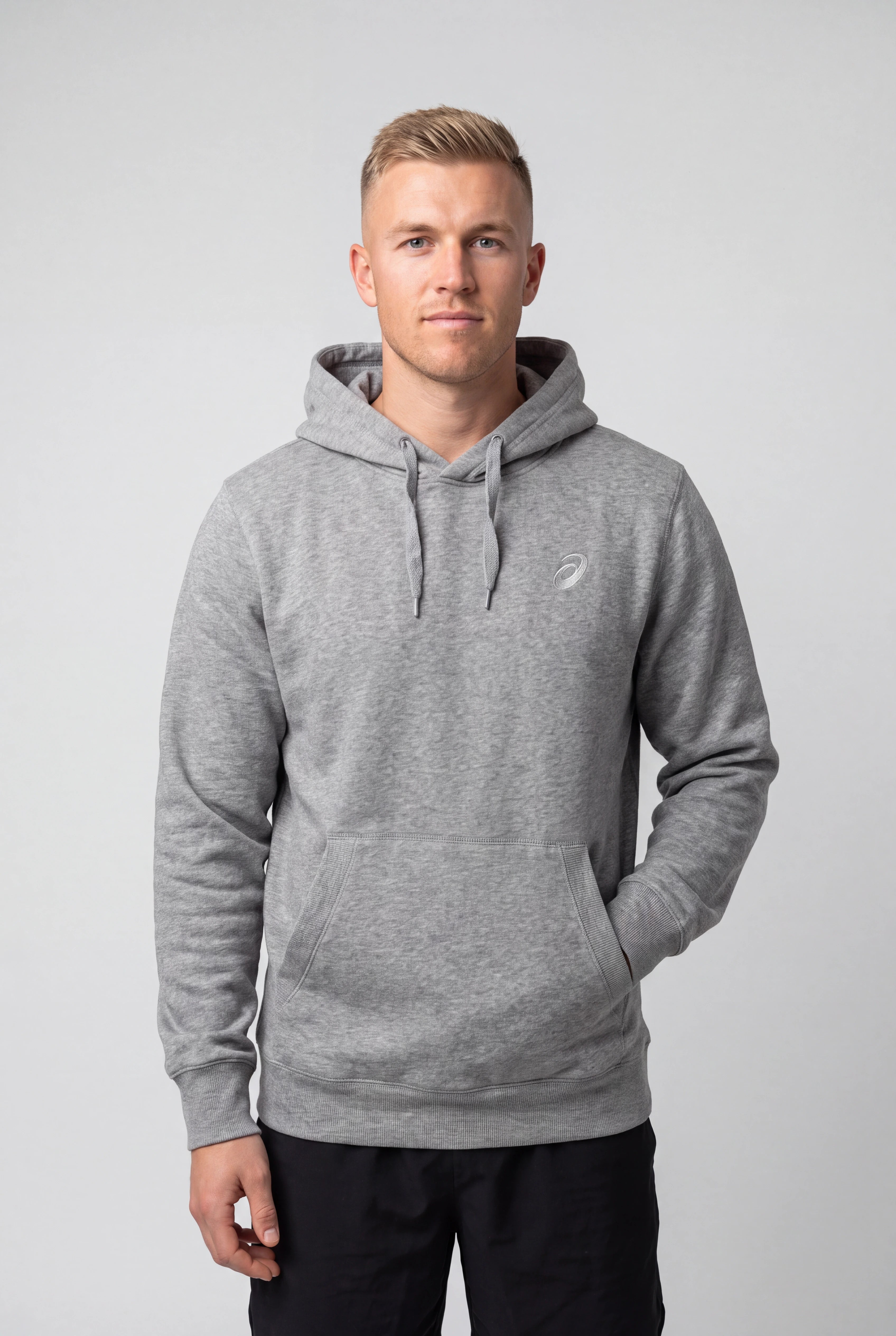 A man wearing a heather gray pullover hoodie with a small white embroidered logo on the left chest, standing against a light gray studio background.