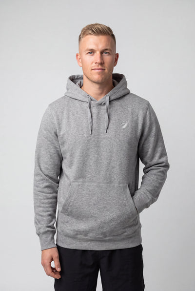 A man wearing a heather gray pullover hoodie with a small white embroidered logo on the left chest, standing against a light gray studio background.