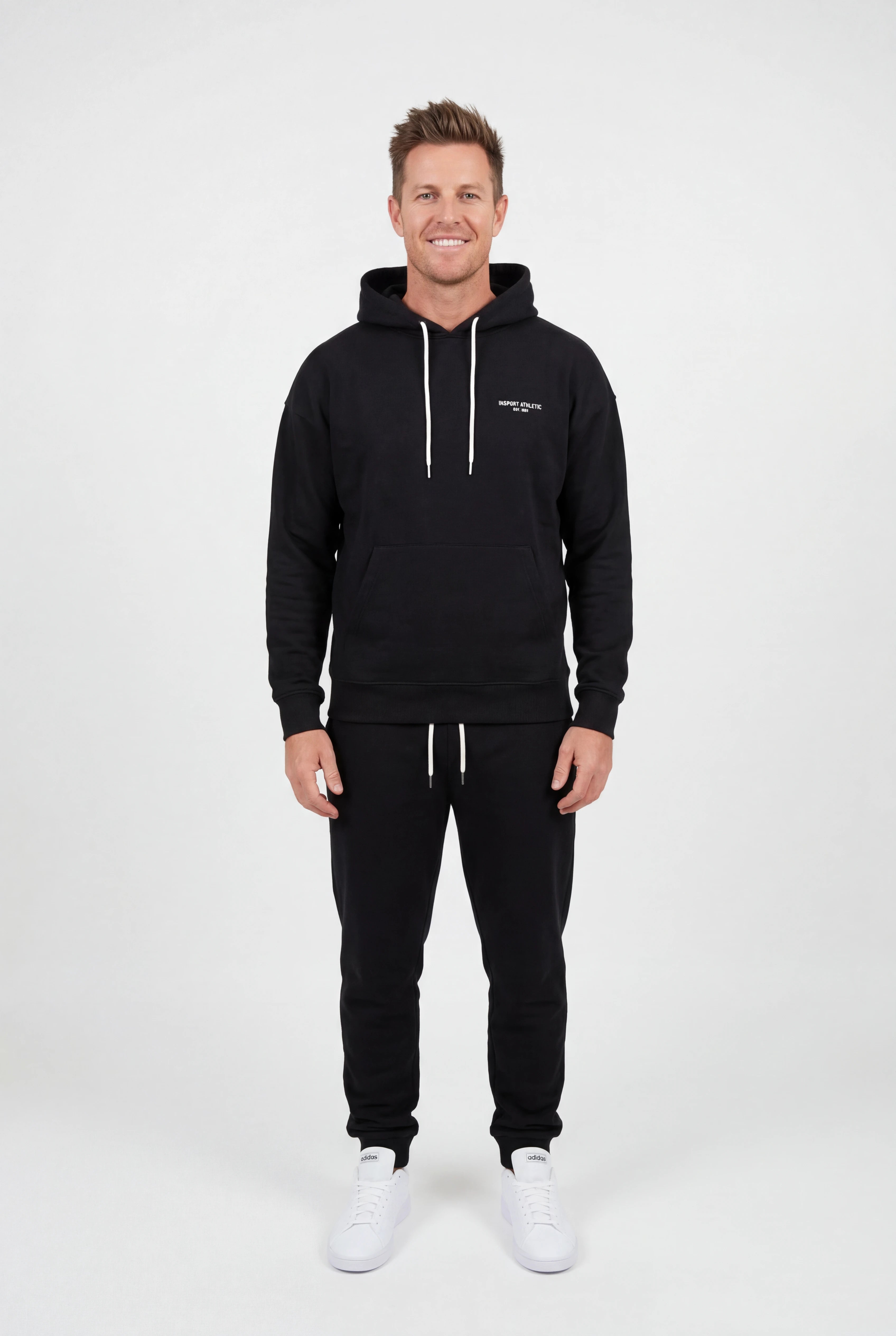 Man wearing a black hoodie and pants with a logo on a white background