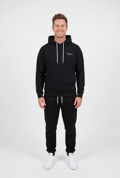 Man wearing a black hoodie and pants with a logo on a white background